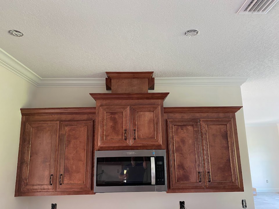 Wooden kitchen cabinets with metal handles, built-in microwave above countertop, light-colored backsplash, hardwood flooring