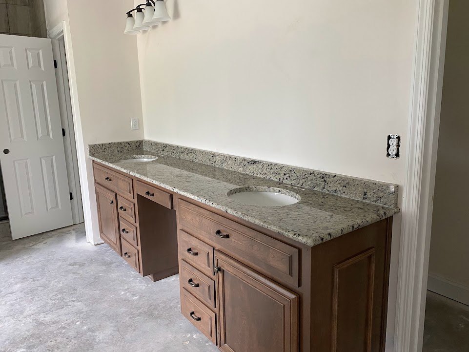 Bathroom with double sinks, white quartz countertop, wooden cabinets, black hardware, white door, and modern white light fixtures above the vanity