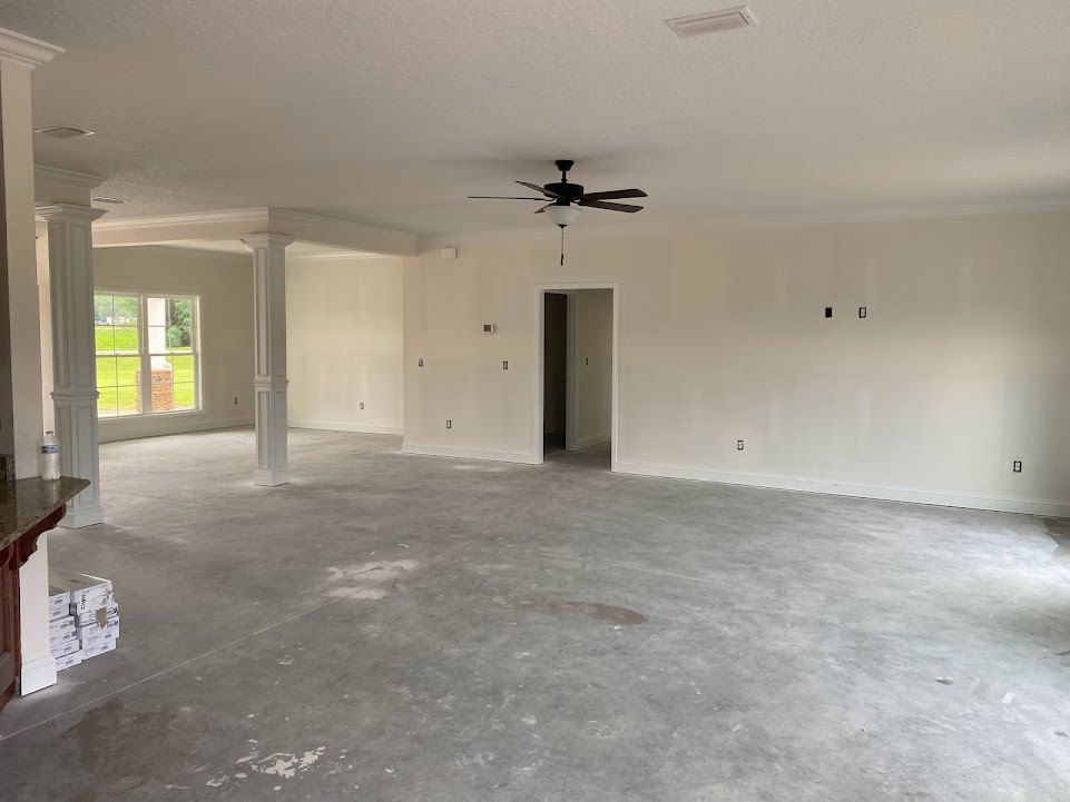 Ceiling fan with light fixture, white walls, grey flooring, window with white frame, white door and light switch, square-based white pillar
