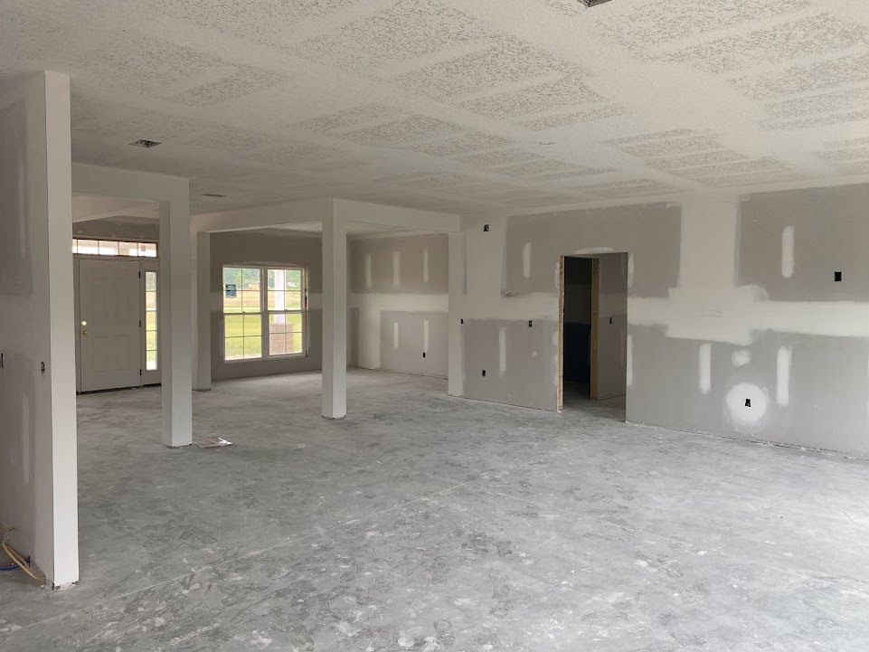 White-walled room with a white ceiling, grey flooring, white pillars, a white-framed window, and a white door illuminated by a light.