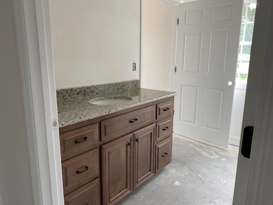 Bathroom vanity with marble countertop, white cabinetry, chrome faucet, and tiled backsplash
