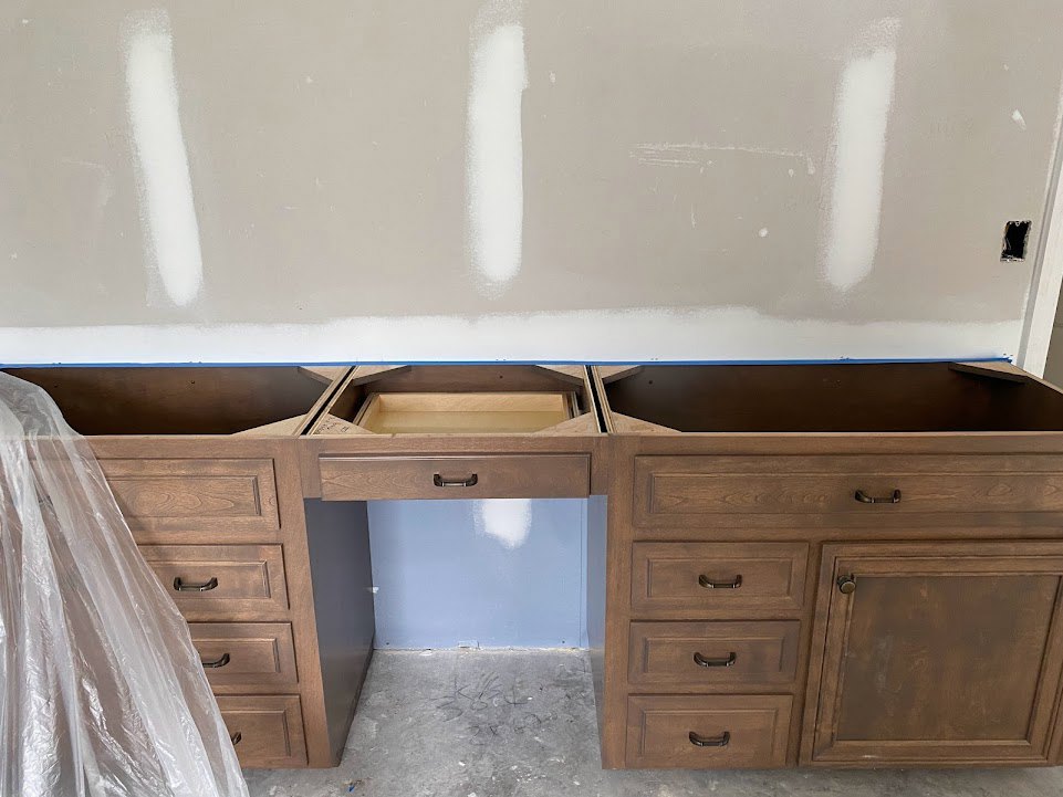 Built-in desk with drawers and open shelf against white painted wall, brown cabinet door with knob, plastic bag hanging from a chair, white object with black handle on desk
