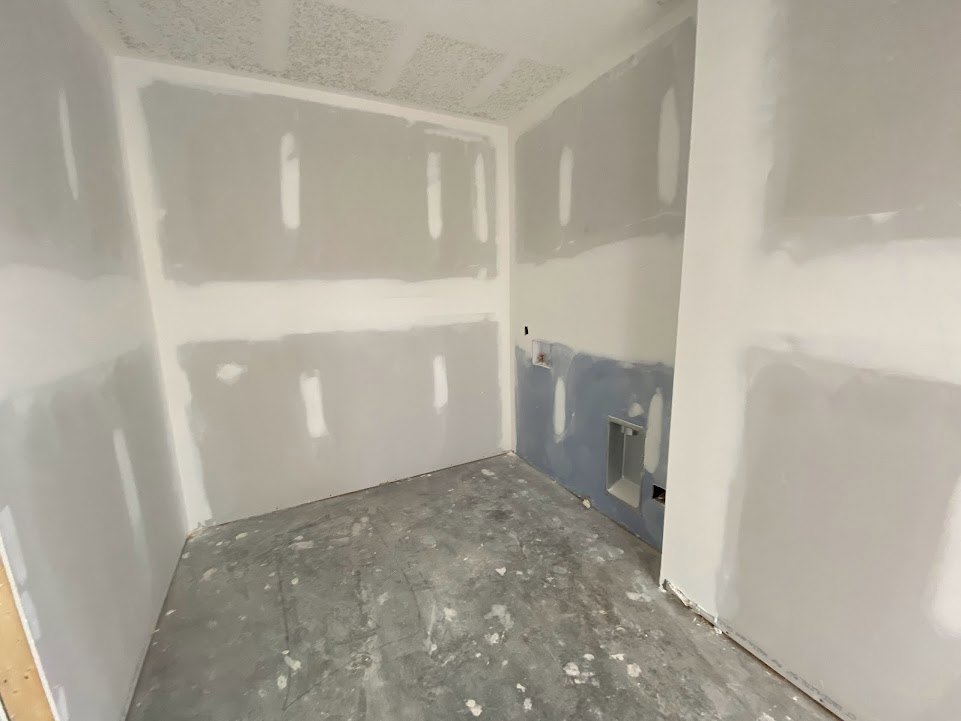 Room featuring white and gray painted walls, gray marble floor with white paint splatters, plaster ceiling, and visible holes in one wall