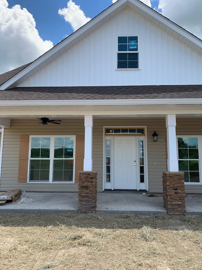 White front door with glass panes, flanked by brick pillars, white-framed windows, and light-colored siding on porch exterior