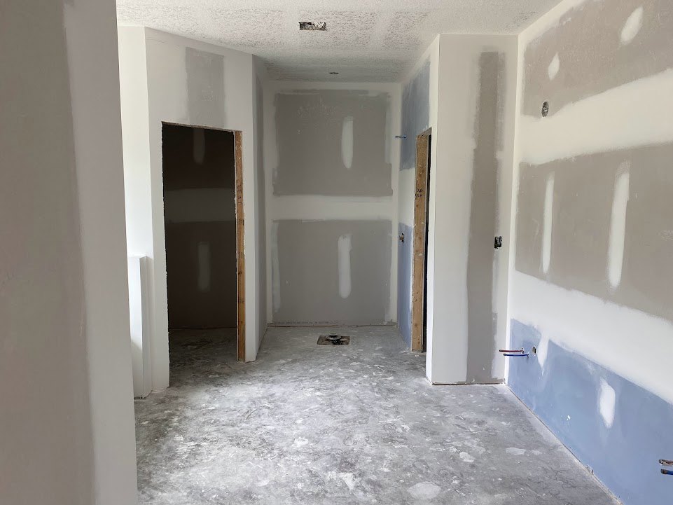White painted walls, light-colored flooring with a floor drain, black rectangular fixture with a white stripe, simple door leading to another space