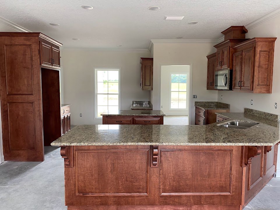 Granite kitchen countertops with white cabinetry, stainless steel microwave above lower cabinets, tile backsplash, window with white frame, undermount sink