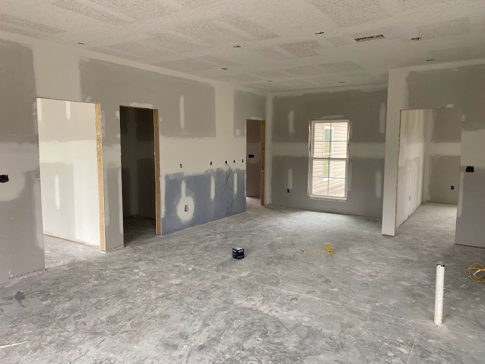 White-walled room with wooden trim, multiple doors and windows, light-colored flooring, and a cardboard box placed near the center.