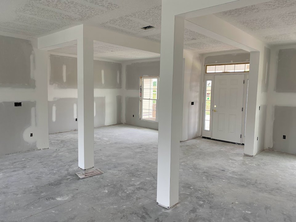 Concrete floor with white pillar, white walls, white door featuring window blinds, and black and white accents in the background