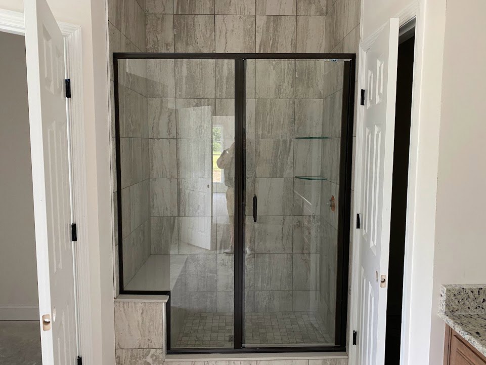 Glass shower door with chrome handle, white and grey marbled tile walls, and countertop in modern bathroom
