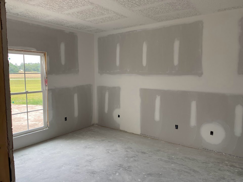 White-walled room with large window overlooking grassy field, smooth concrete floor, and plaster ceiling