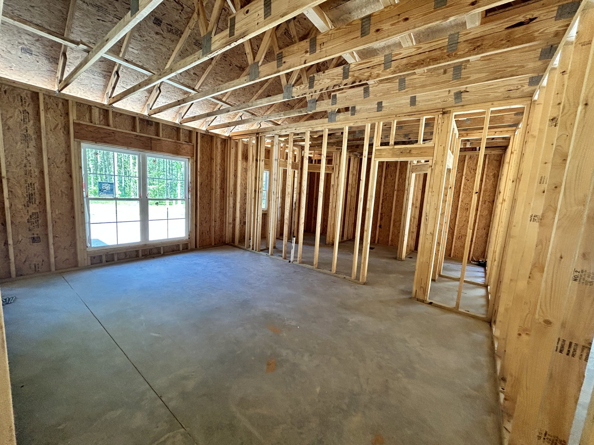 Concrete floor with exposed wood ceiling beams, large window overlooking trees, unfinished walls