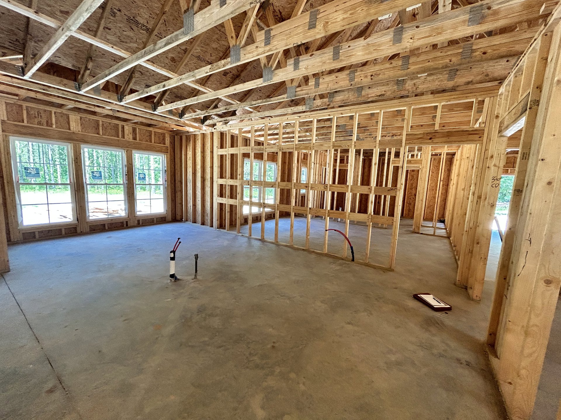 Wood-framed room with exposed beams, concrete floor featuring visible pipes, window with a sign, and pen resting on a paper tray