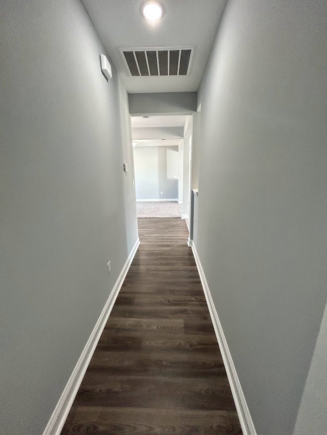 Hallway with light wood flooring, white plaster walls, ceiling vent, and visible staircase railing