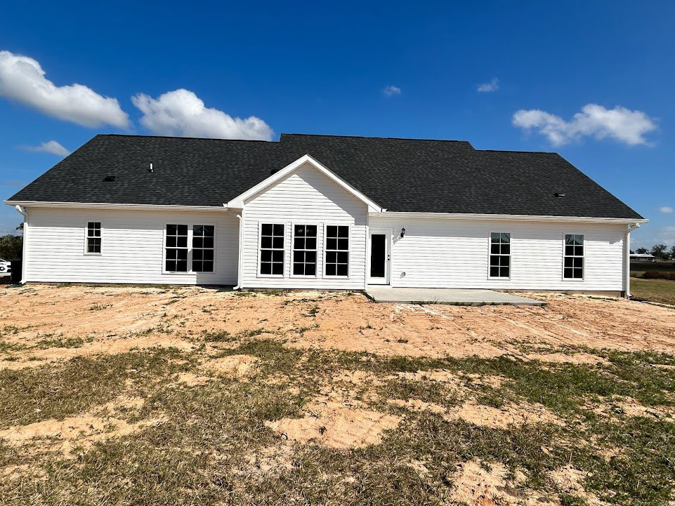 White house with black roof under construction, dirt foreground, multiple square windows, blue sky overhead