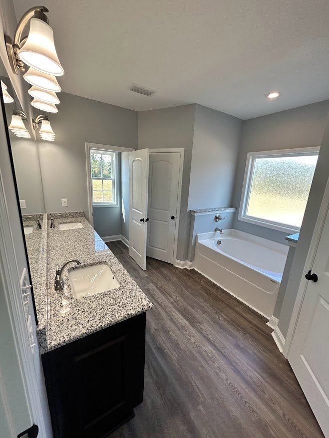Bathroom featuring a marble countertop with a white sink and chrome faucet, freestanding bathtub, frosted glass window, light cabinetry, and laminate flooring