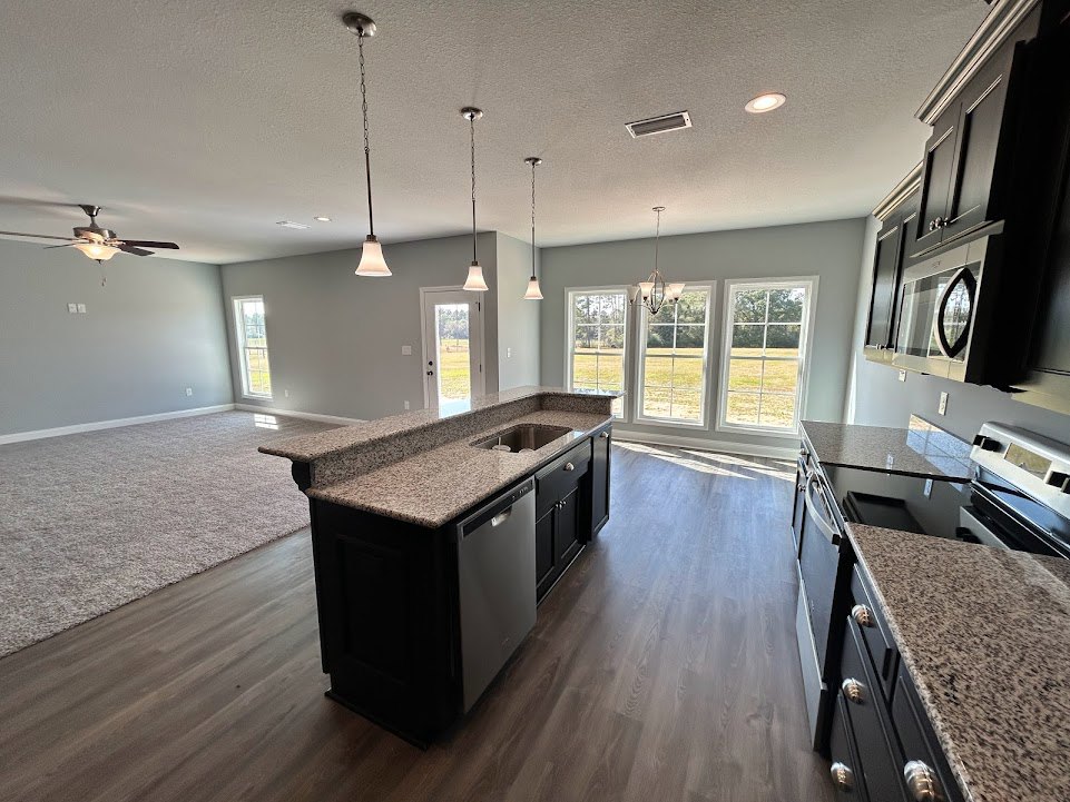 Open-concept kitchen and living room featuring a large window, granite kitchen island with black speckled countertop, white walls with black trim, light cabinetry, and hardwood