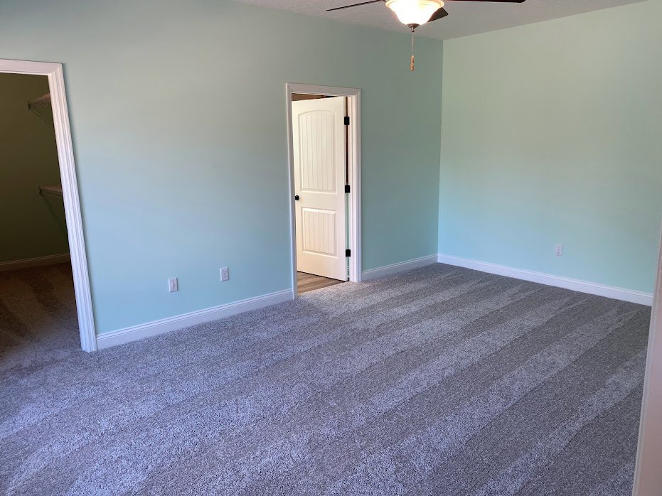 White paneled door with black hardware opening into a carpeted room, white door frame, textured plaster walls, ceiling light fixture with pull string.