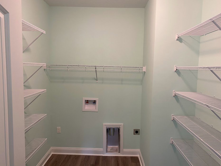 White built-in shelves on a plaster wall, wood flooring with white baseboard, small dog door inset near the floor, metal cup and colored objects on shelves.