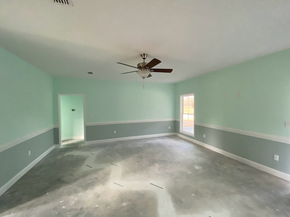 Concrete floor room with white plaster walls, ceiling fan with light fixture, and white-framed window.