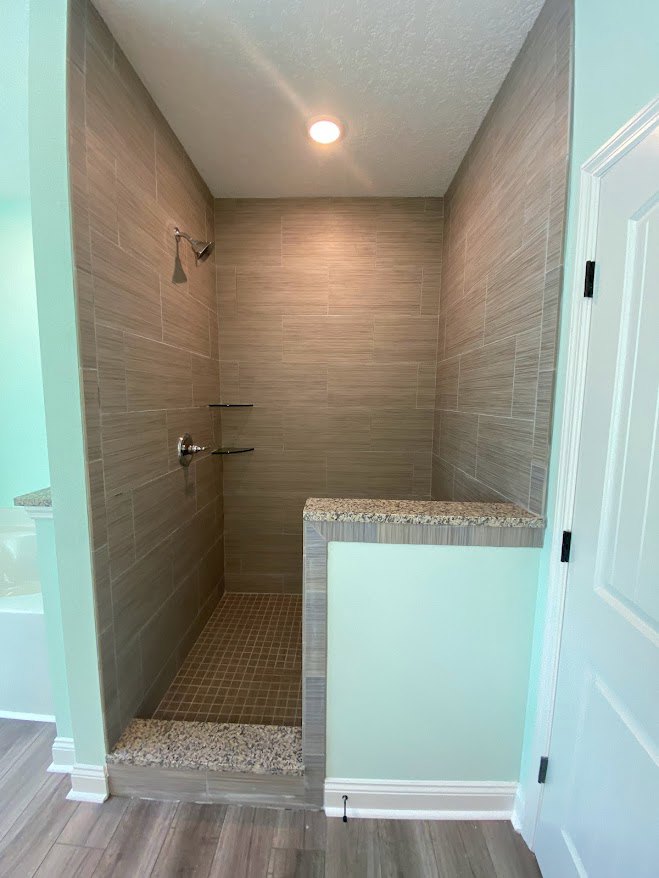 Brown tile shower floor with white walls, black door handle, and blue accent background