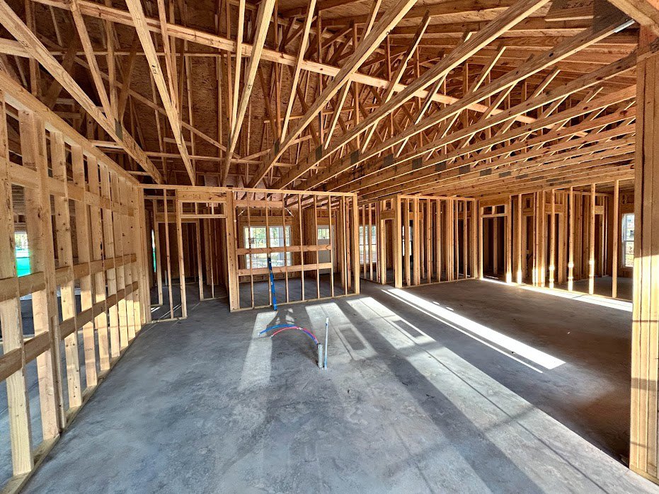 Concrete floor with red and blue pipes, exposed wooden beams and framing, unfinished ceiling, house under construction