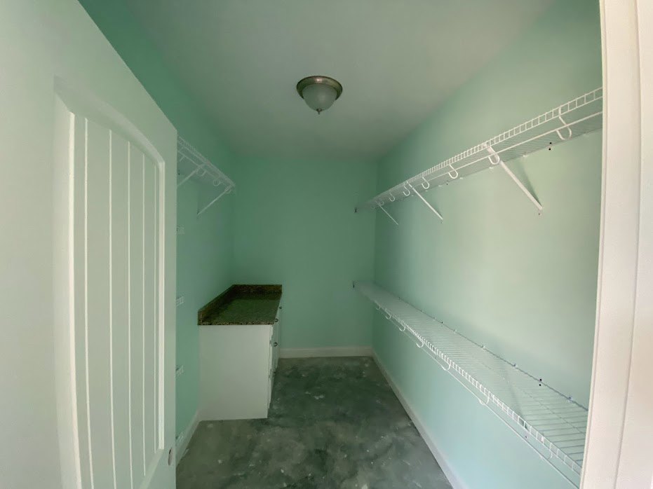 Built-in white shelves and cabinets along a plaster wall, recessed lighting fixture above, light-colored floor with visible dirt, door and molding detail in a modern bathroom