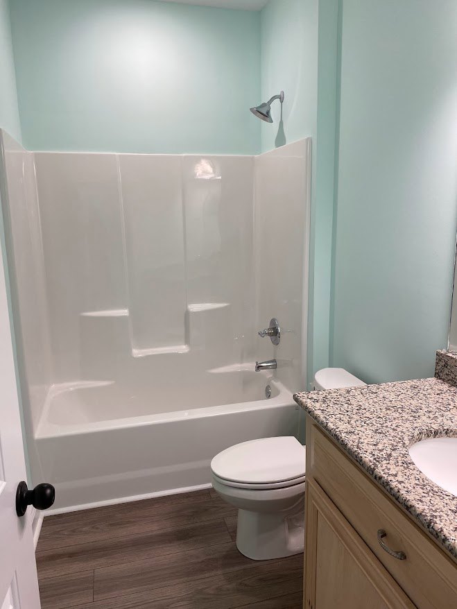 Bathroom with white toilet, rectangular sink set in stone countertop, freestanding white bathtub, wood flooring, and light-colored tile walls