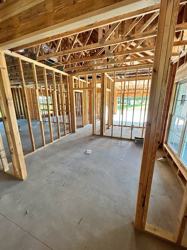 Living room with exposed wood ceiling beams, white-framed window, light hardwood floors, and neutral walls.