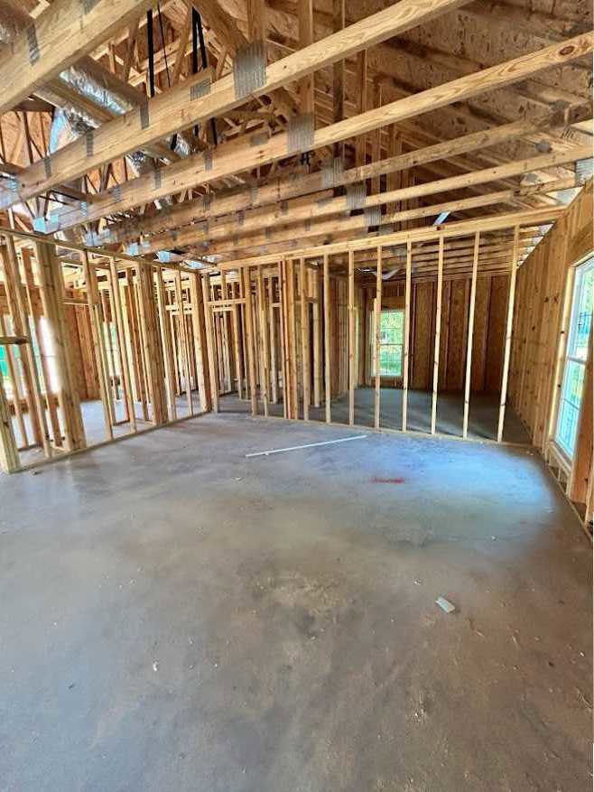 Exposed wooden ceiling beams, concrete floor, large window showing blue sky, unfinished wood framing