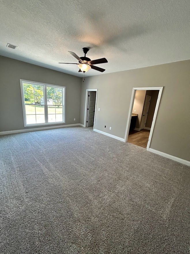 Bright room with laminate flooring, white plaster walls, ceiling fan with light, large window overlooking green trees