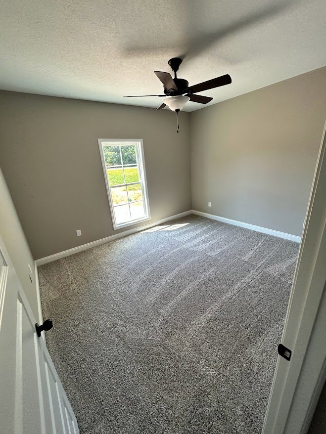 Carpeted room with white plaster walls, ceiling fan with light fixture, and neutral interior finishes