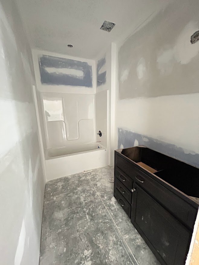Bathroom featuring a freestanding white tub, black cabinet with drawer, grey countertop with white accent line, and dark wood cabinetry against plaster walls and tiled floor