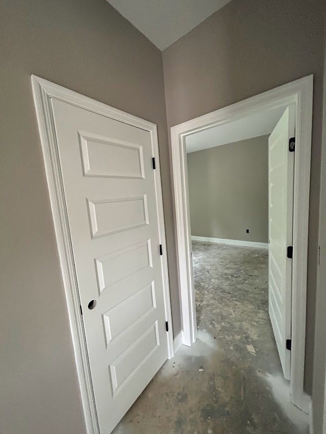 White paneled door with round hole in center, black object in corner, concrete floor, white baseboard trim, light gray walls