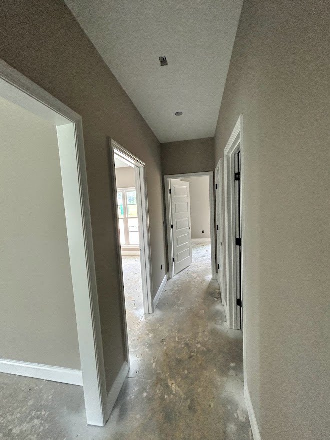 Hallway with smooth concrete floor, white paneled doors featuring black hinges, plaster walls, and natural light from a nearby window