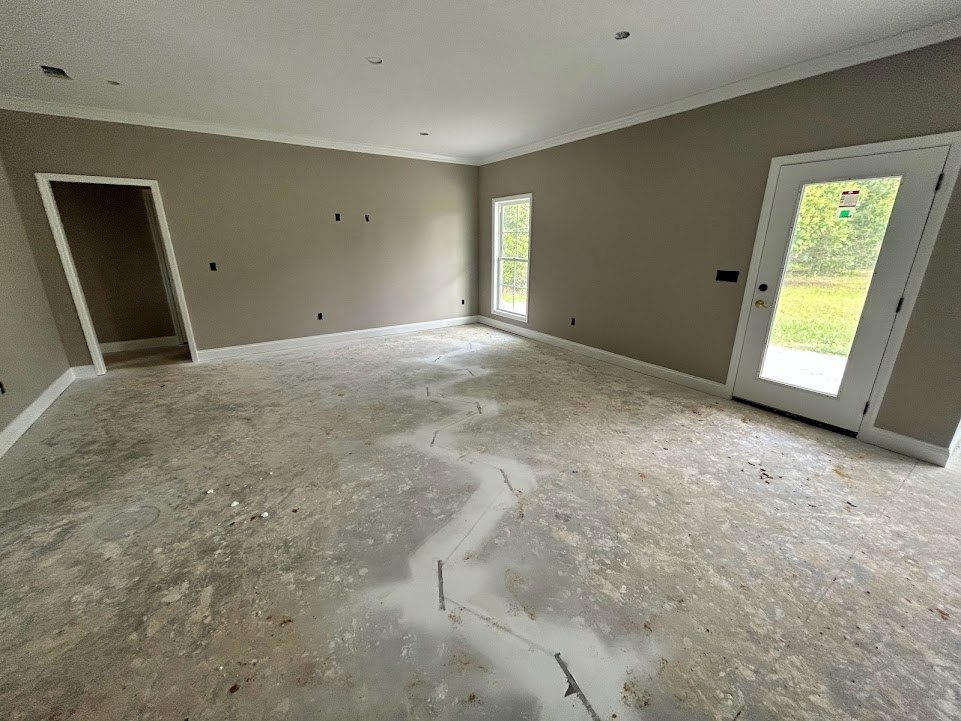 Concrete floor room with white walls, white door featuring a glass window, and a white-framed window.