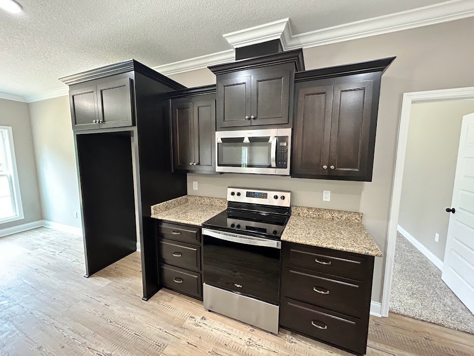 Modern kitchen featuring a built-in microwave oven with glass door above a black and silver stove, black cabinetry with white countertop, white curtain covering a window, and
