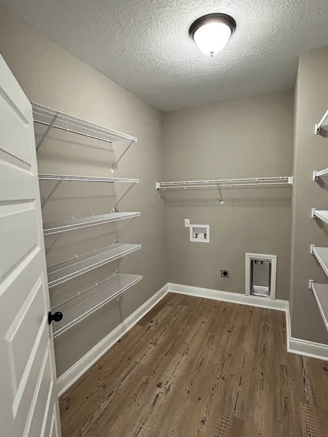 Built-in white shelves along a plaster wall, wood flooring with white base trim, recessed ceiling light, white door, chrome water faucet near cabinetry