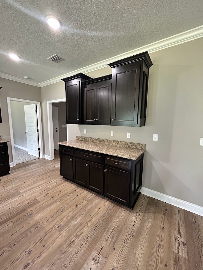 Kitchen with dark wood cabinets, marble countertop, wood flooring, and white door with black hardware