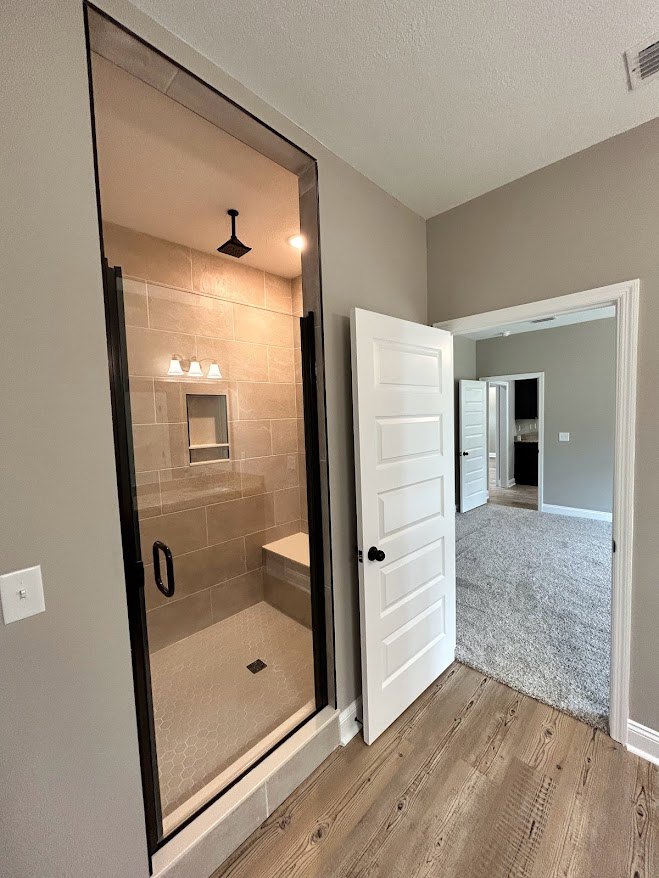 Bathroom with glass shower door, white entry door featuring black knob, light tile flooring, plaster walls, and recessed ceiling lighting