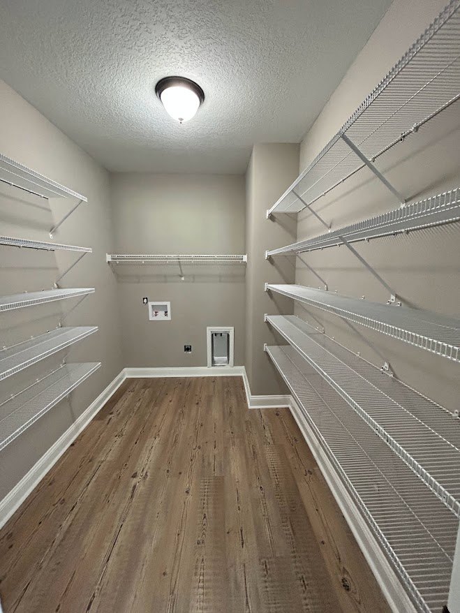 Spacious walk-in closet with wood flooring, white baseboards, built-in metal shelving, and a ceiling-mounted light fixture