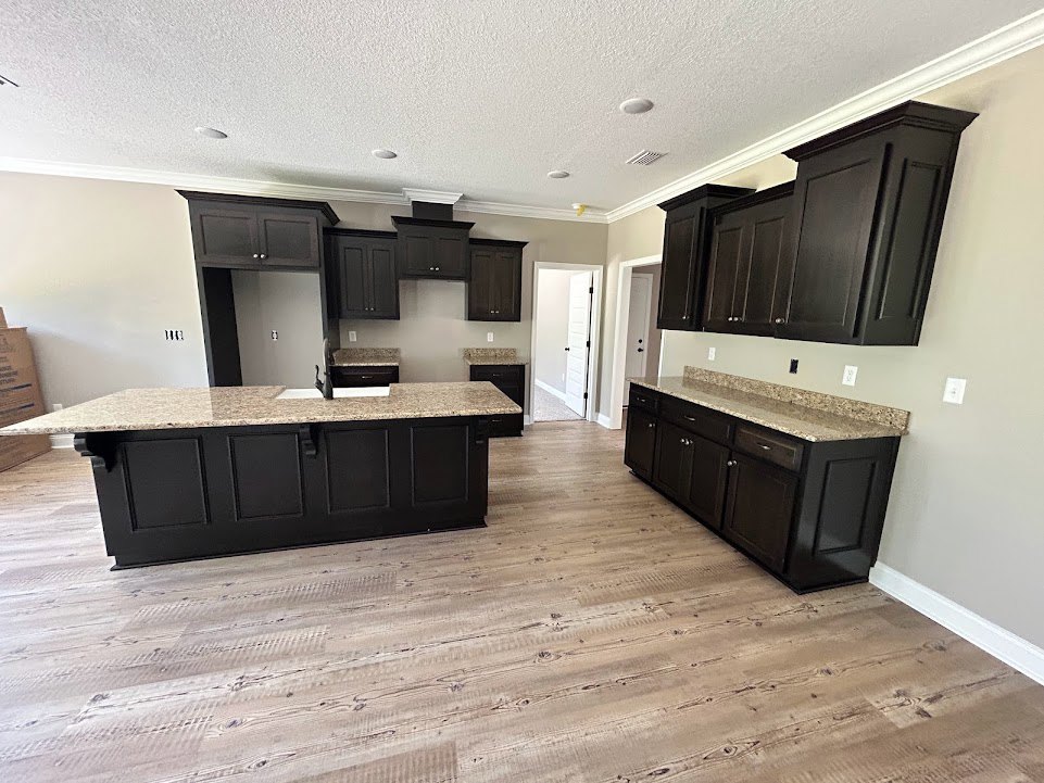 Kitchen with black cabinets, granite countertops, black kitchen island with marble top, wood flooring, white door with black knobs, stainless steel sink, and tile backsplash.