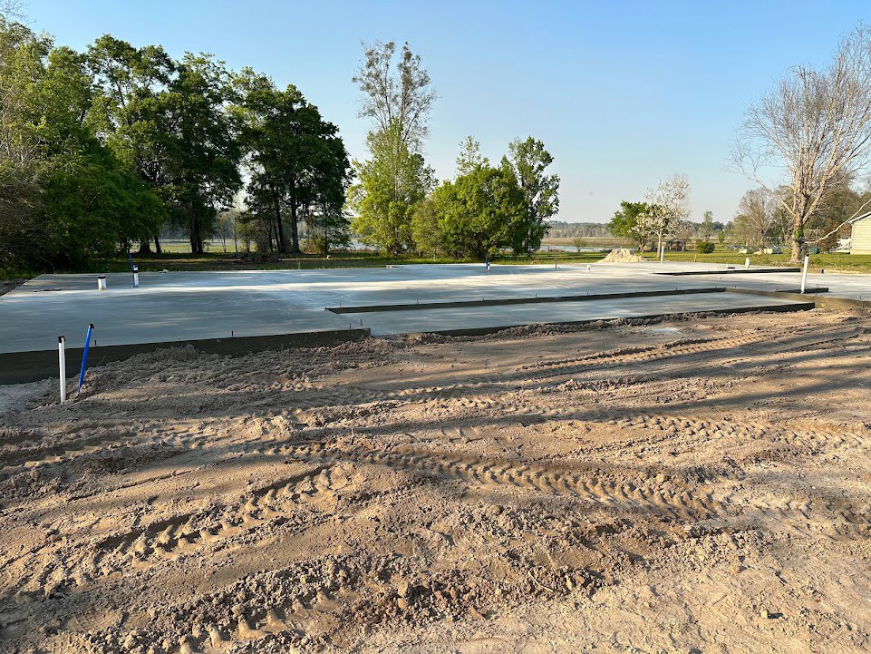 Dirt road with visible tire tracks, bordered by a mix of leafless and green trees under an open sky