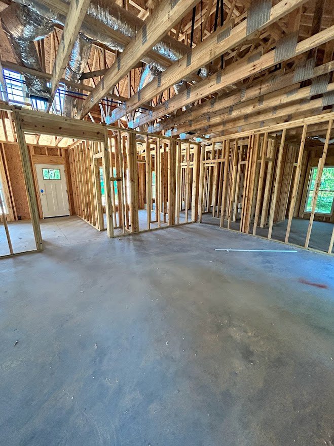 Exposed wood ceiling beams, unfinished wood framing, white door with sign, green glass window, visible ducts and insulation on ceiling, bare subfloor