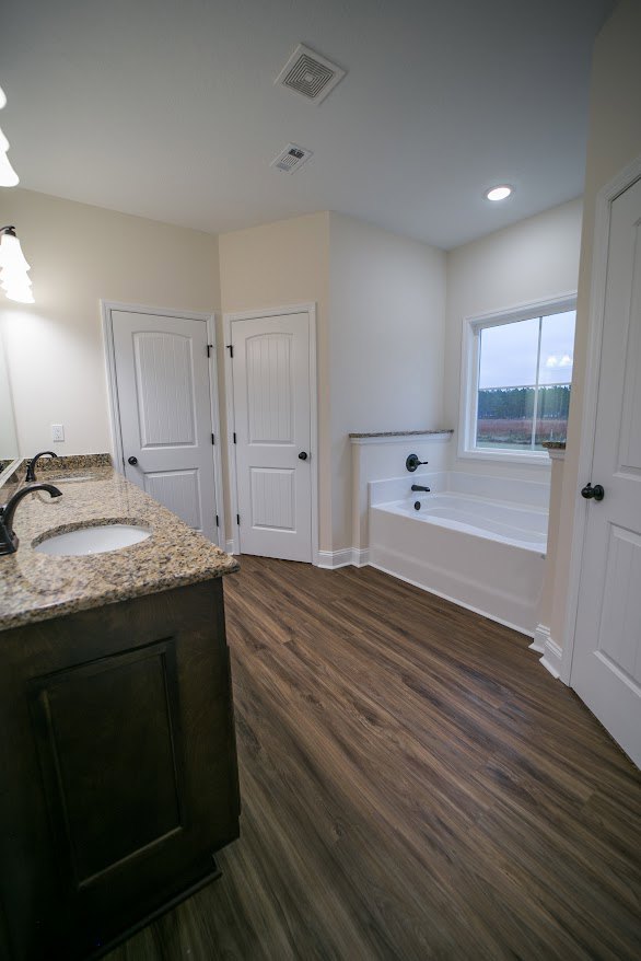 Bathroom featuring a marble countertop, freestanding bathtub, wood flooring, white walls, white door with metal knob, ceiling vent, and modern sink with chrome faucet