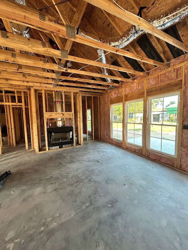 Living room with exposed wood beams, large windows, concrete floor, glass door fireplace, and view of neighboring house.