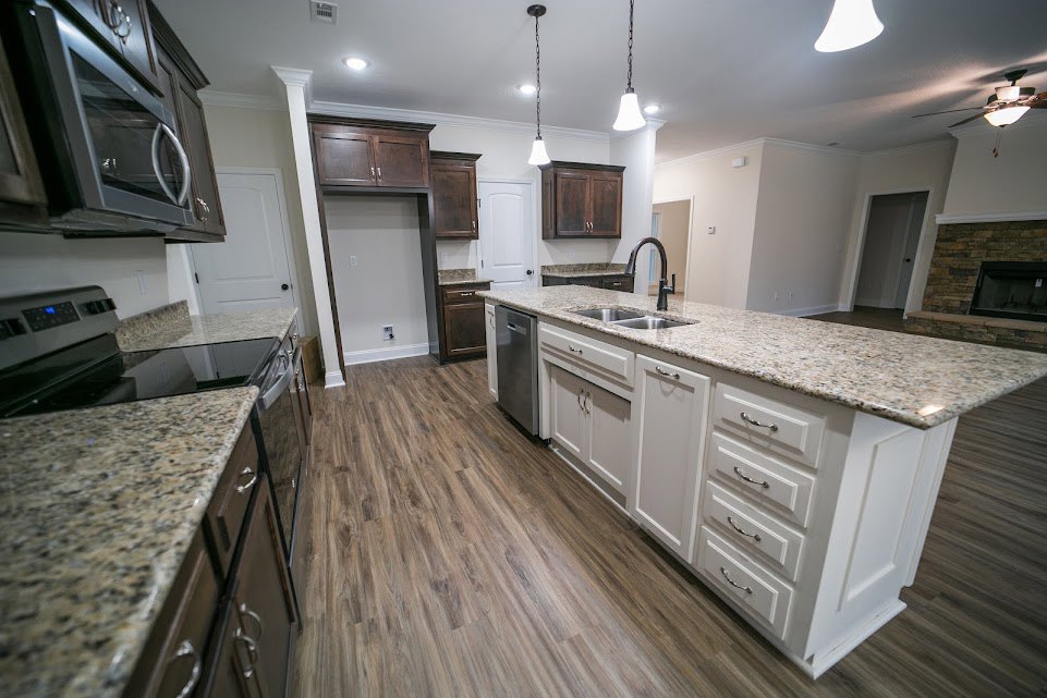 Granite countertops, stainless steel sink, white kitchen island with drawers, built-in microwave, pendant ceiling lights, white cabinetry, white door with black knob
