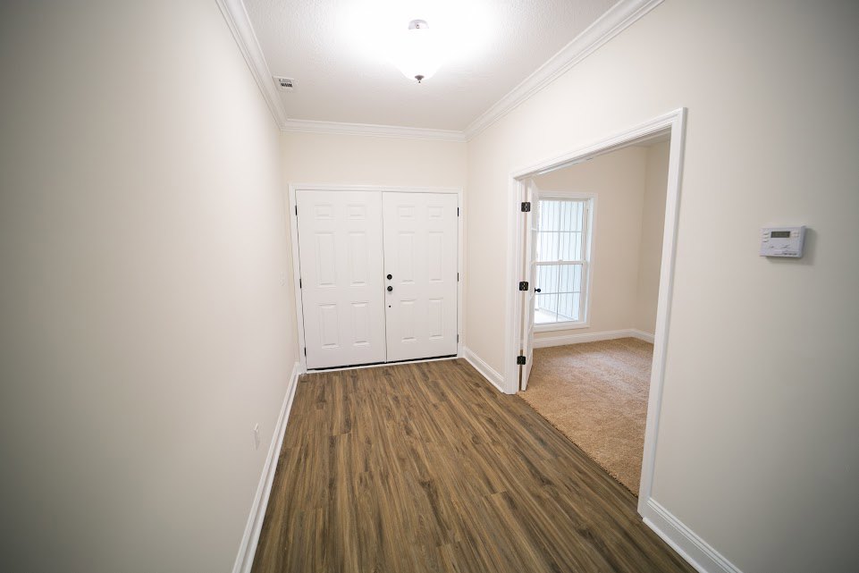 Hallway with white paneled doors featuring black knobs, hardwood flooring, white walls, ceiling light fixture, and a carpet runner