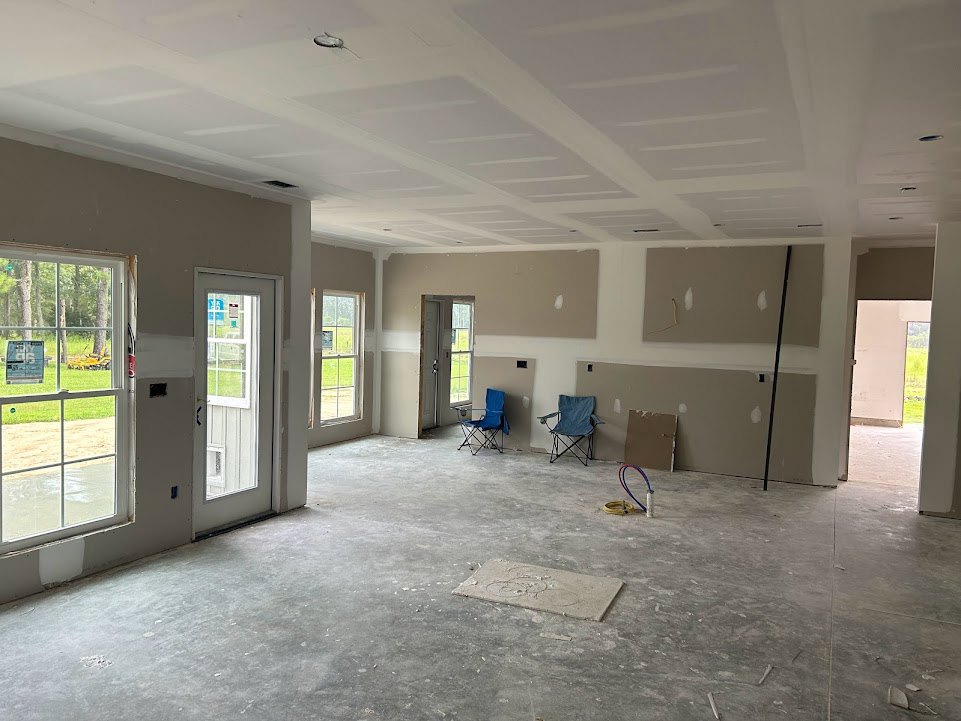 Blue folding chair positioned against a white plaster wall, glass door with window and signage, concrete flooring, and ceiling fixtures in a residential interior room