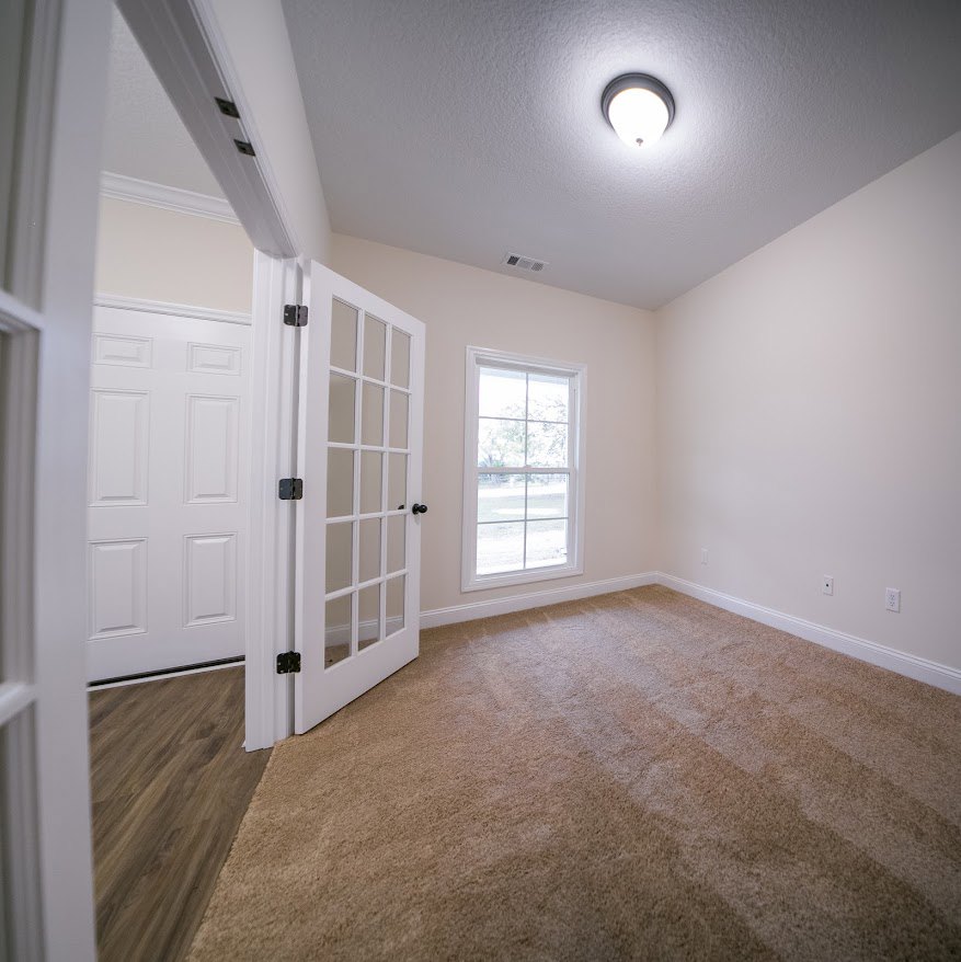 Carpeted room featuring a white paneled door with black knobs, multi-pane window, white walls with crown molding, and ceiling-mounted light fixture