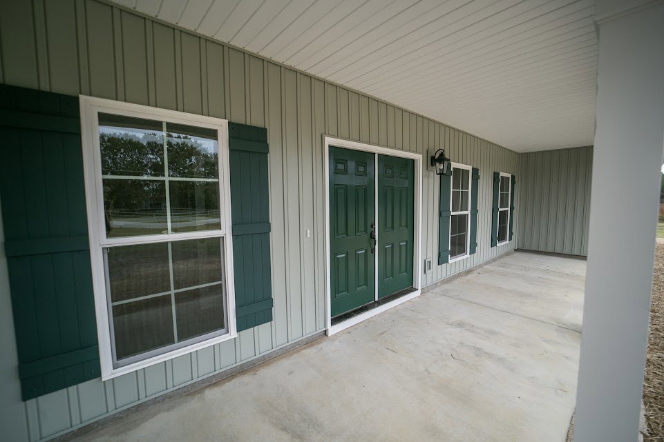 Green double front door with white trim, adjacent white-framed window, concrete floor leading to entry, exterior facade featuring multiple green doors and windows.